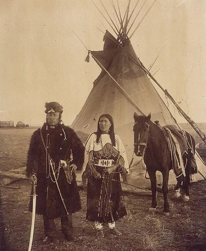 A historical photo shows a Native American couple in traditional attire with a horse and tipi, capturing a past moment.