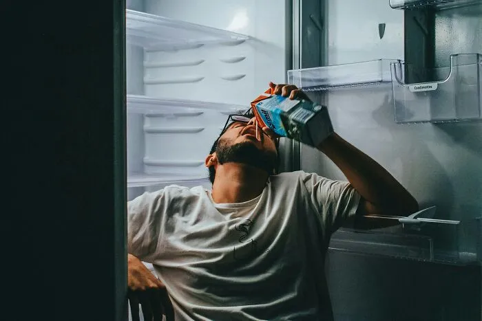 A person drinking directly from a carton inside a fridge, depicting the disturbing aspects of internet rabbit holes and cults.