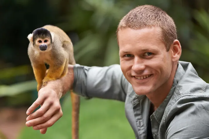 A smiling man with a squirrel monkey on his arm, showcasing interaction and guest house etiquette.