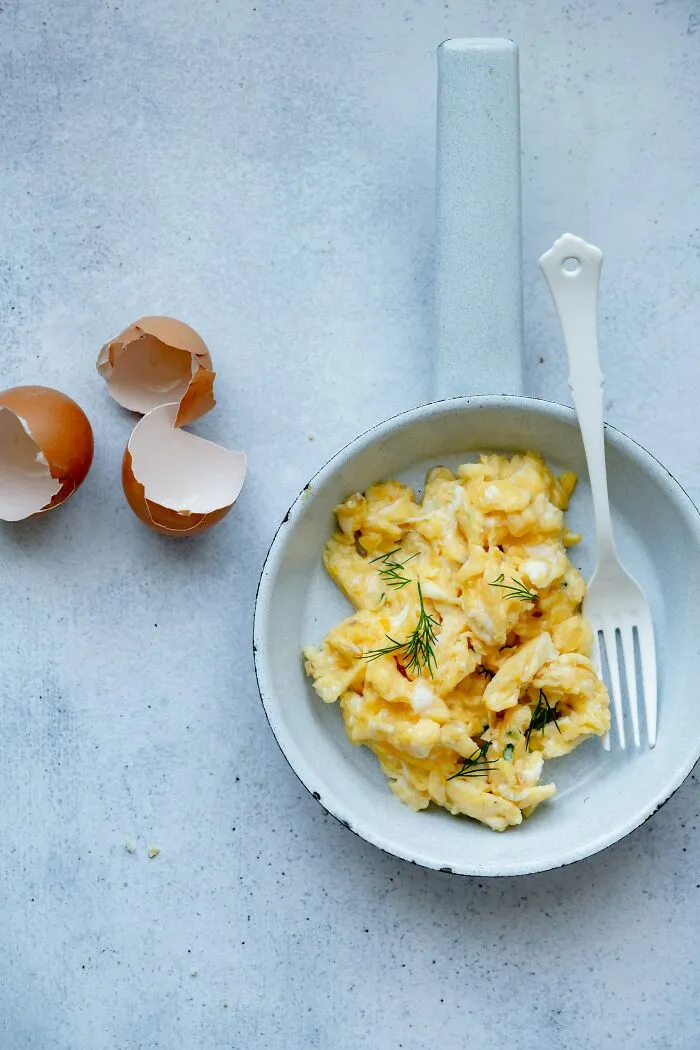 Scrambled eggs in a pan with eggshells beside it, a secret companies might not want you to know about food prep.