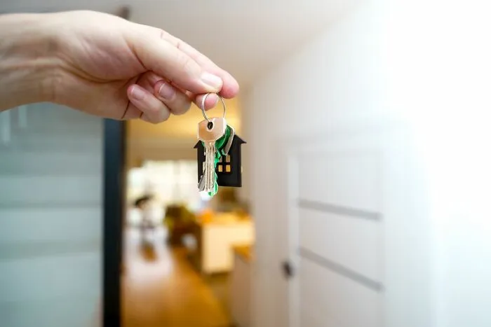 Hand holding house keys with a house-shaped keychain, symbolizing behind the scenes secrets in real estate companies.