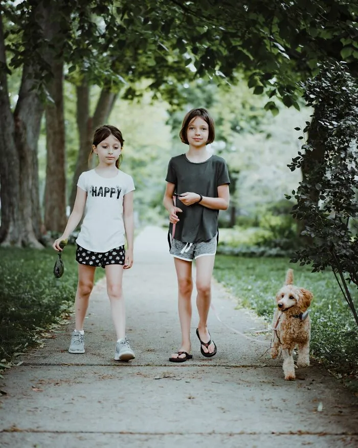 Two young children and a dog walking on a path, a parent capturing a moment of their children being happy.