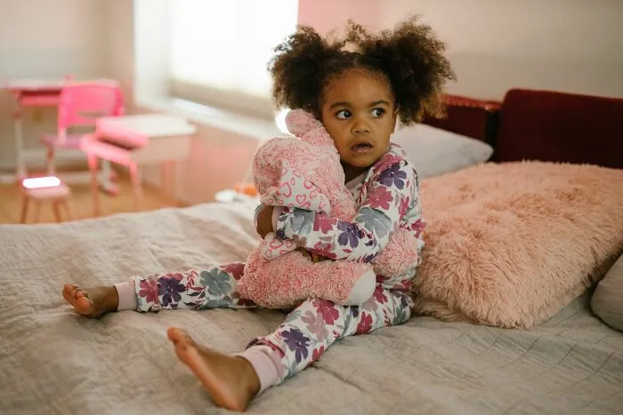 A young child in pajamas, clutching a stuffed animal, with a look of worry that could make parents terrified.