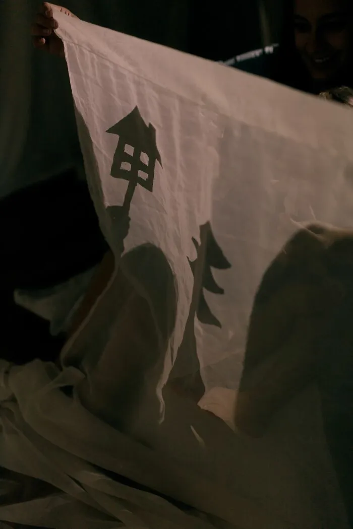 A person holding up a translucent sheet with shadowy figures, creating a sense of being terrified of their own children.