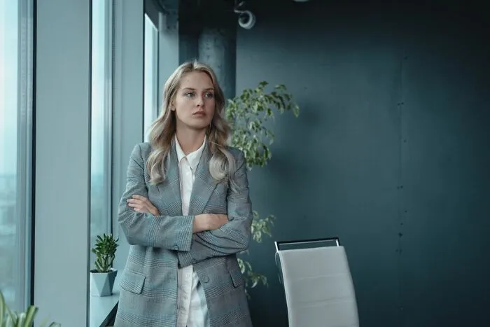 A pensive businesswoman with crossed arms, reflecting on entitled friends and their true colors.