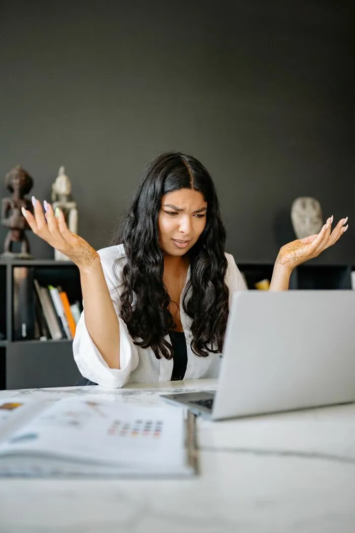 A woman at a laptop shrugging in confusion, illustrating the bewilderment caused by entitled friends.