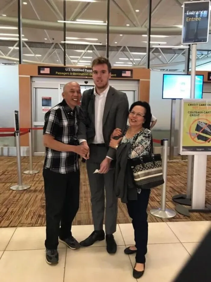 A tall man in a suit posing for a photo with two older people at an airport, highlighting moments people asked celebrities for a photo.