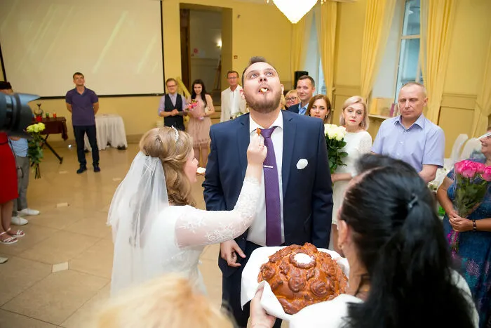 A funny wedding photo of a bride feeding the groom in front of guests.