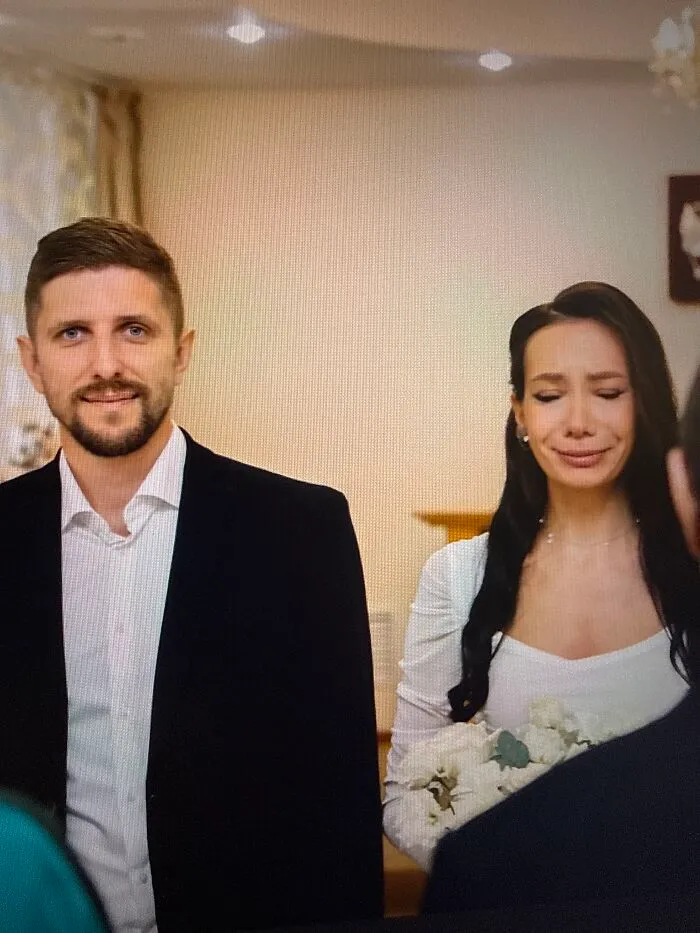 A silly wedding photo of a groom smiling while his bride stands beside him with a crying face.