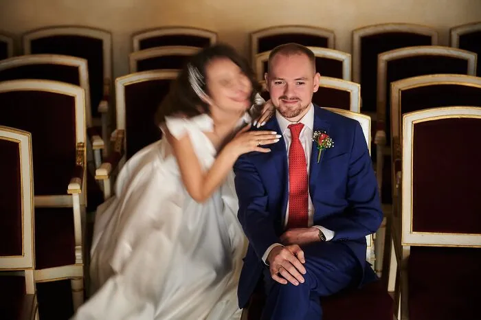 A blurry bride embracing a focused groom in a blue suit with a red tie, capturing a funny wedding photo.