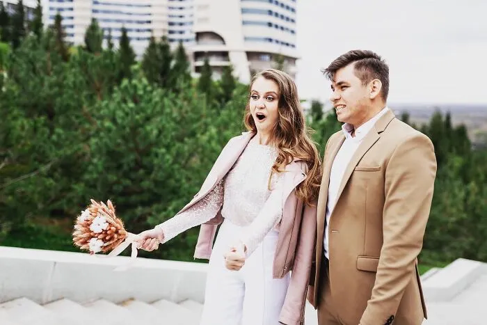 A bride with an open mouth expression and a groom looking sideways, capturing a funny wedding photo outdoors.