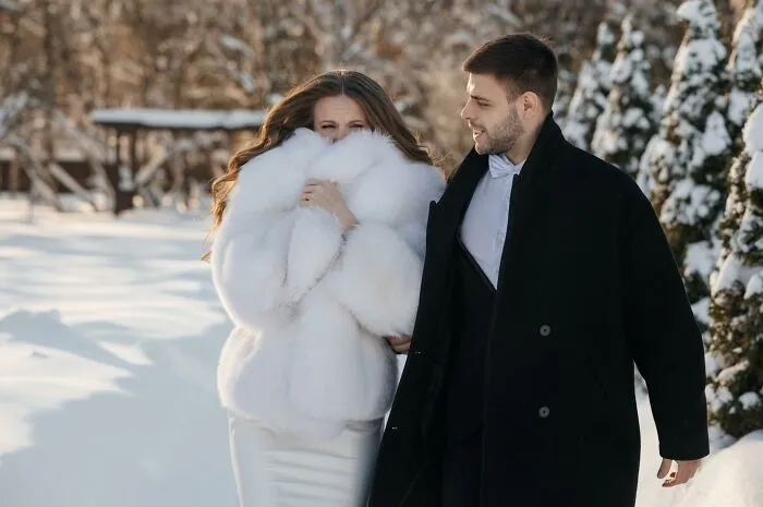 A couple walking in the snow, the bride in a white fur coat, a funny wedding photo capturing a silly winter moment.