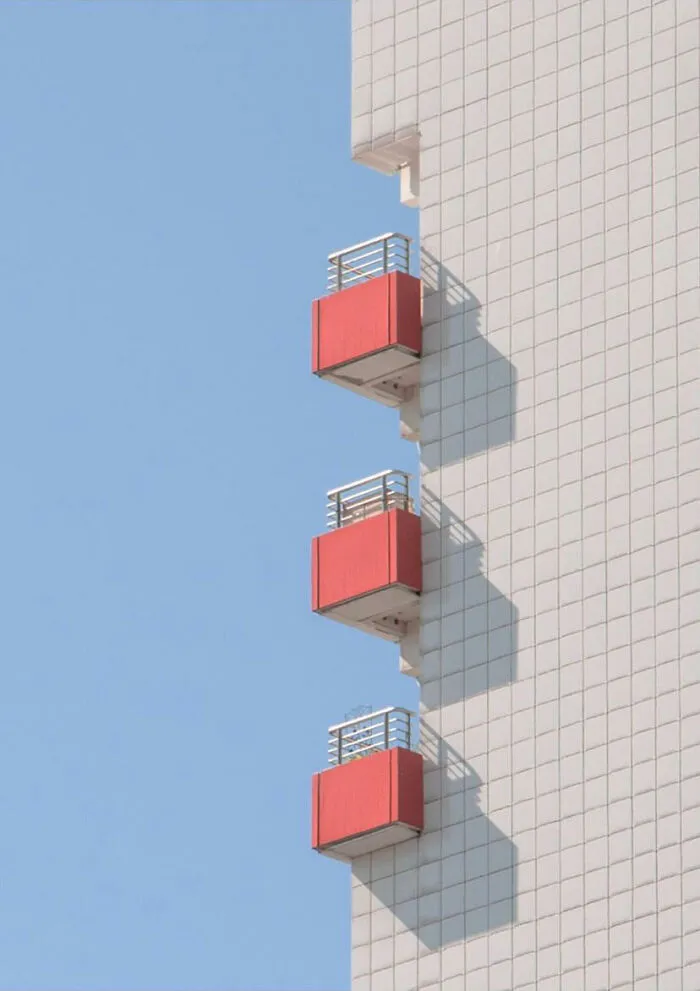 A minimalist photography of a building with three red balconies against a clear blue sky, emphasizing simplicity.
