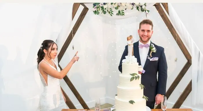 Bride pointing at groom next to a tall wedding cake, creating a funny wedding photo.