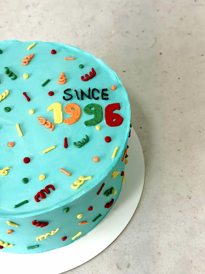 A light blue cake decorated with colorful sprinkles and the words Since 1996. Bakers prove treats look amazing and taste delicious.