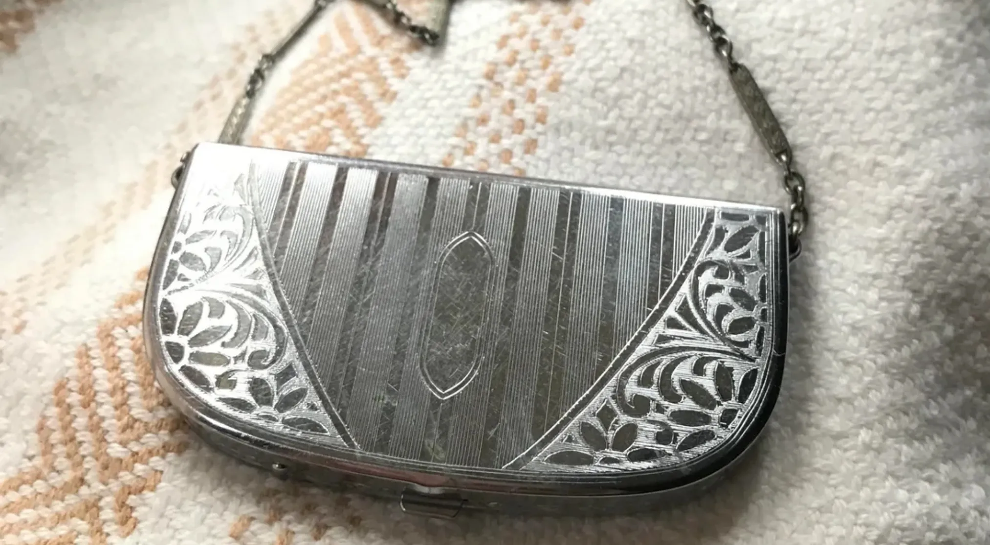 A metallic vintage item, a small purse or case with intricate etched floral designs and vertical stripes.
