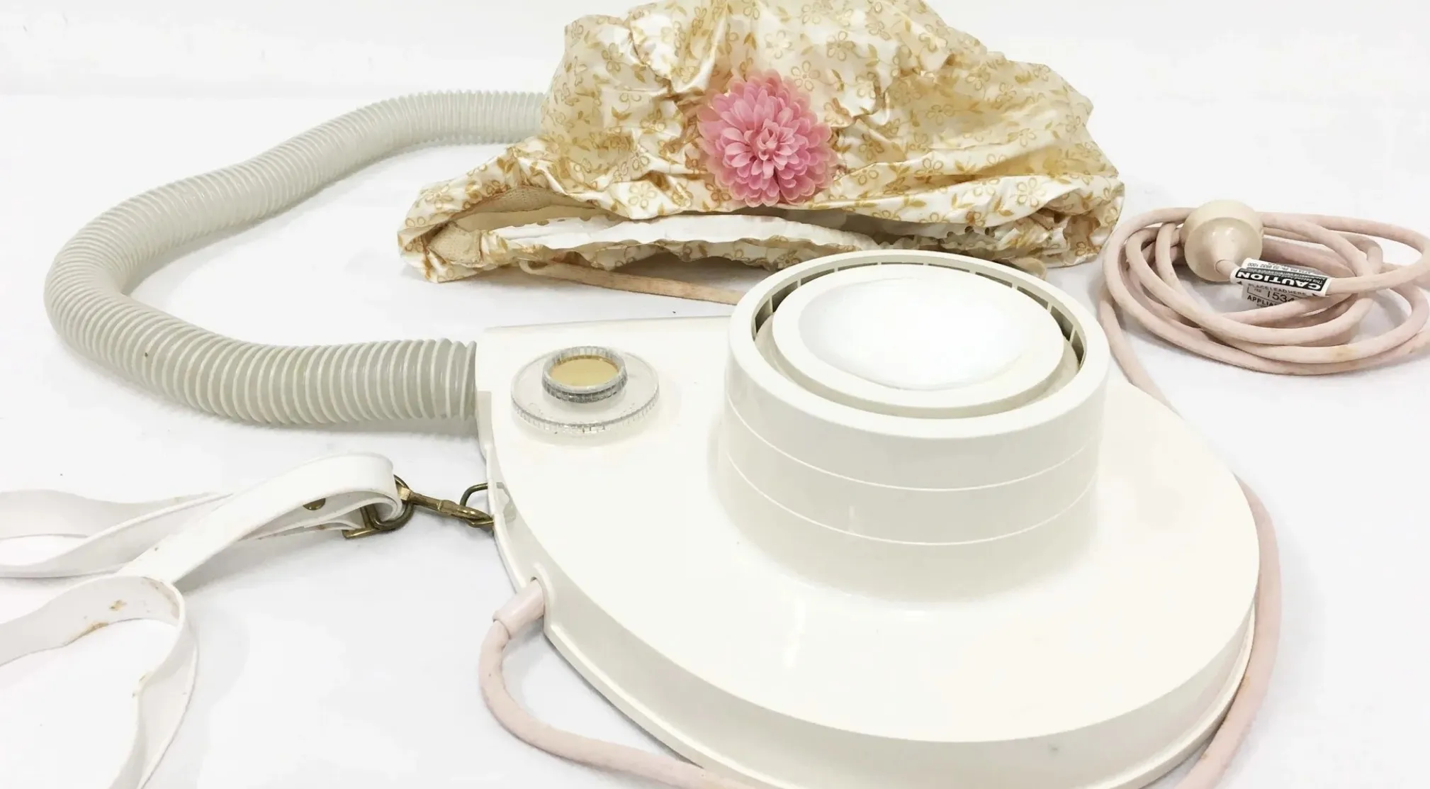 A vintage item: a portable bonnet hair dryer with a patterned bonnet, hose, and base, on a white surface.