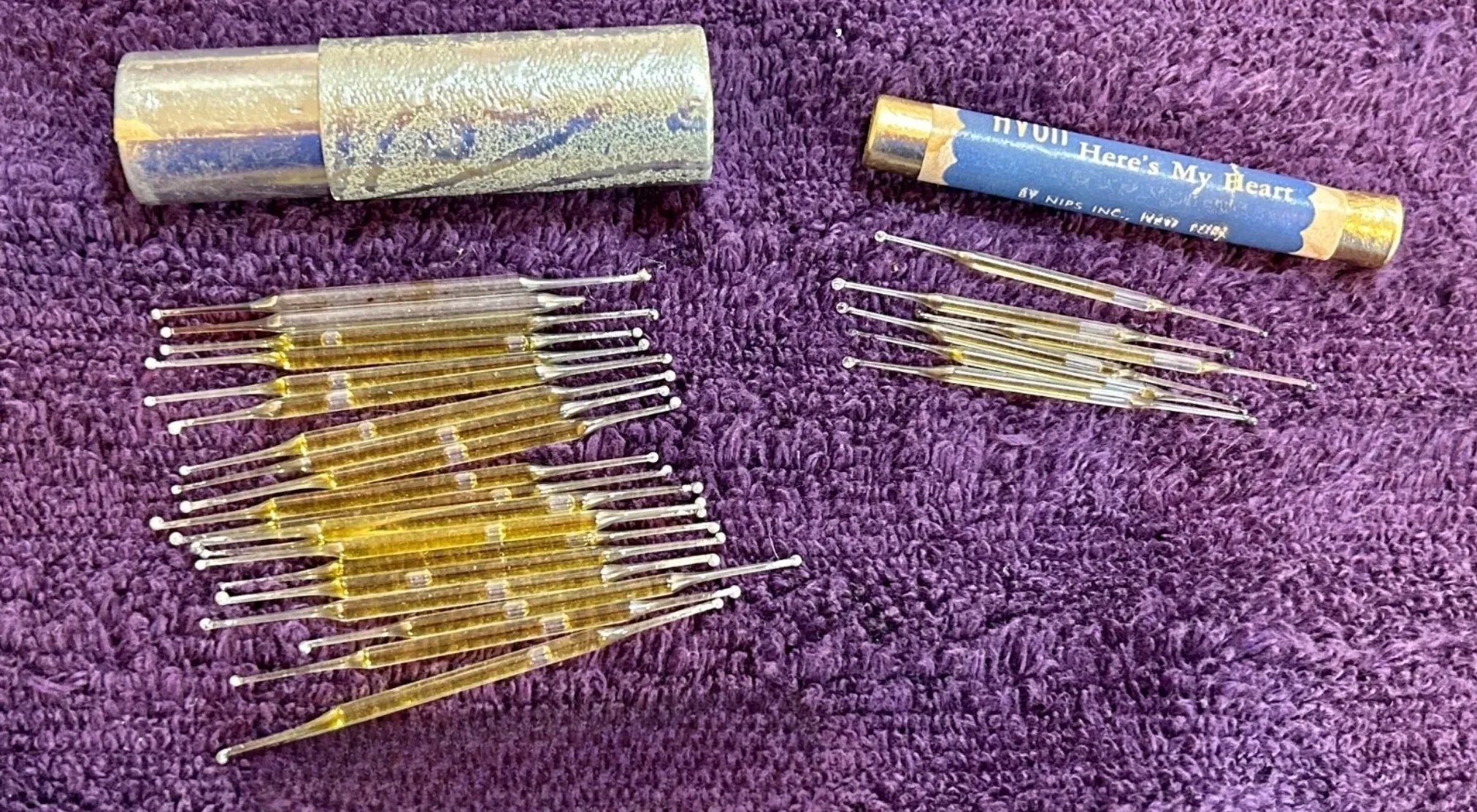 A collection of vintage items on a purple textured surface: two cylindrical cases and several small glass tubes. Guess the vintage item.