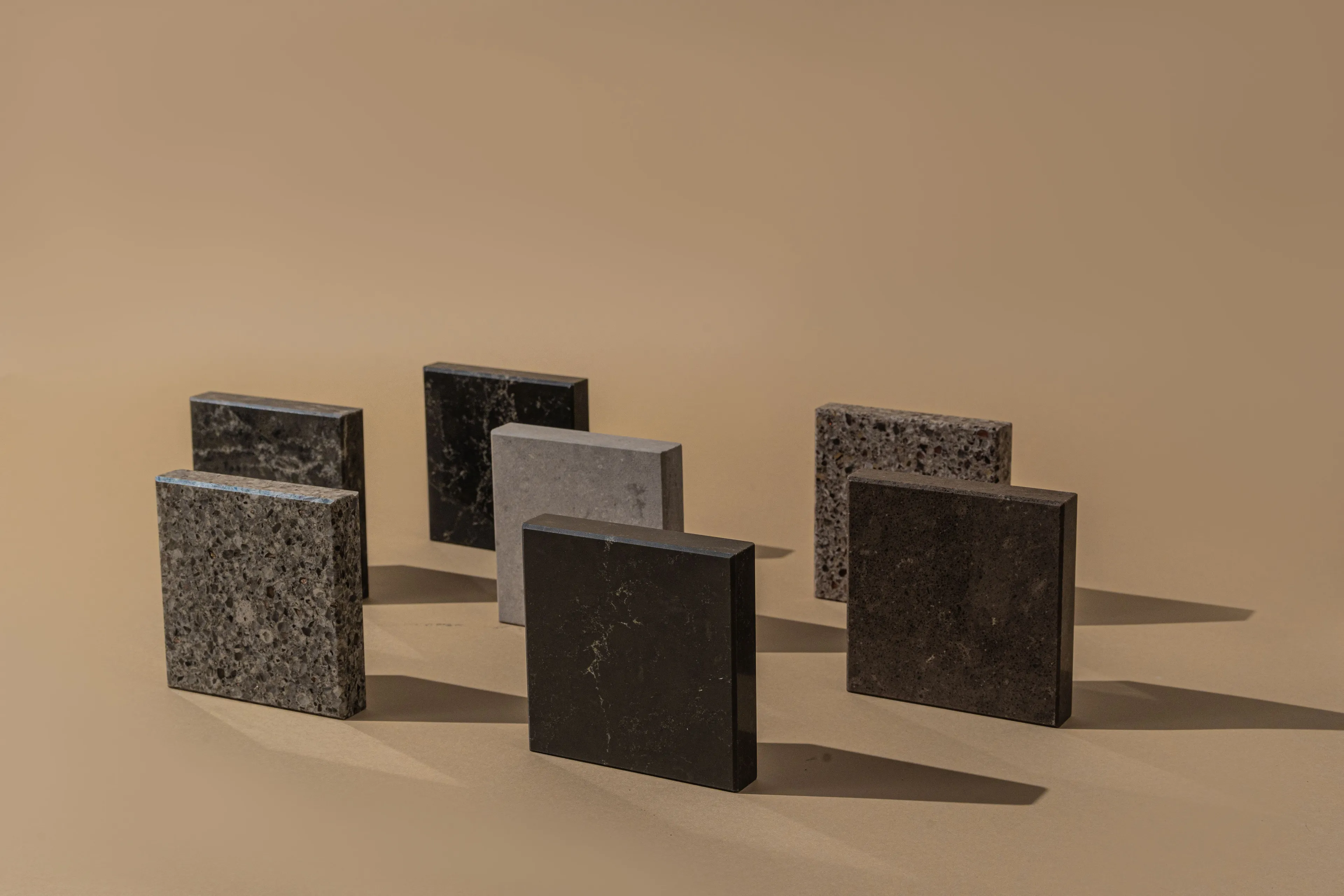 Several Japanese cube samples in varied dark materials like granite and marble, casting shadows on a beige background.
