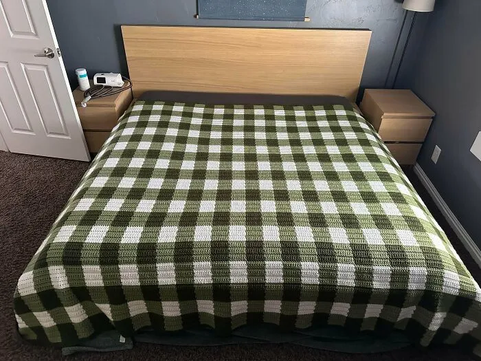 Green and white crochet blanket with checkered design on bed