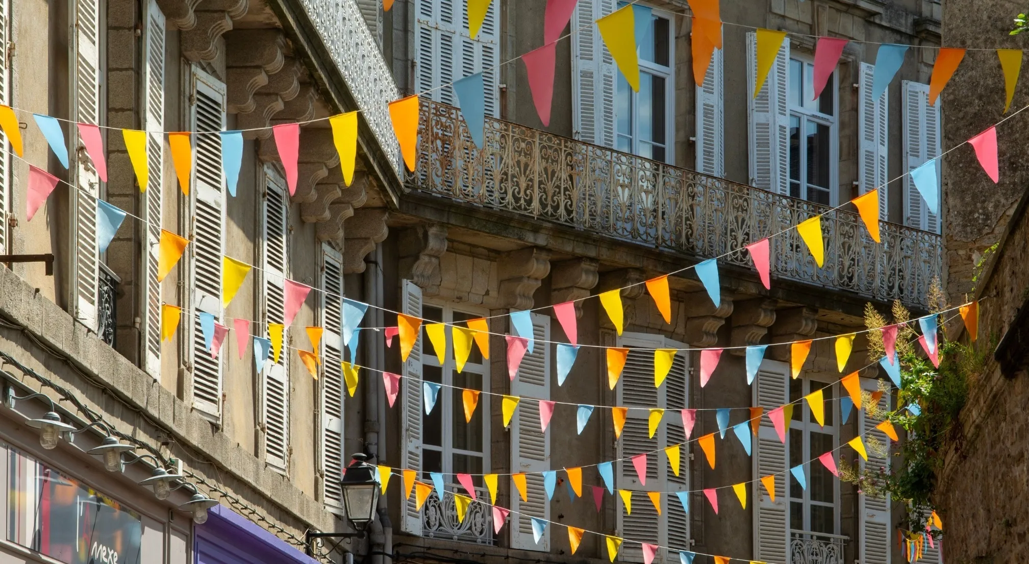 Decorative arrangements of colorful bunting flags strung across a narrow street in a European town with old buildings.