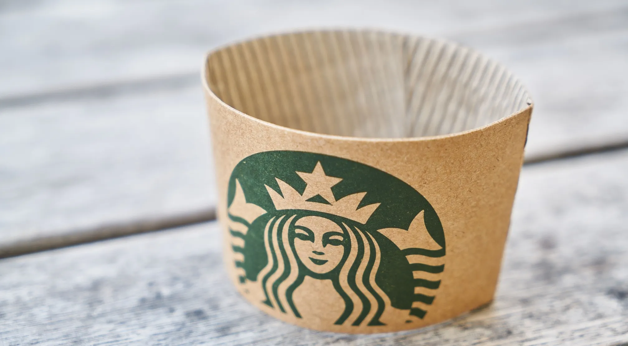 Close-up of a Starbucks coffee accessory, a brown cup sleeve with the iconic green siren logo, resting on a wooden surface.