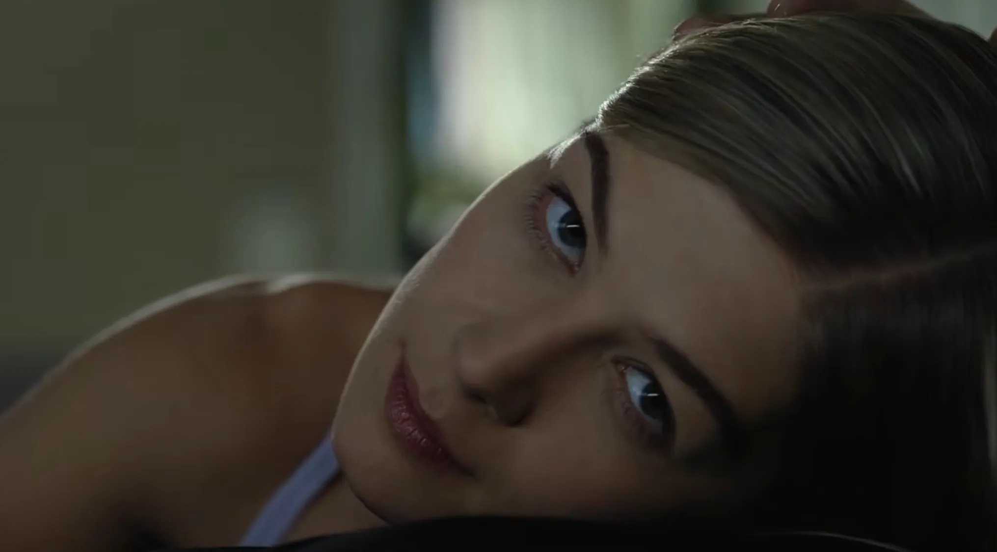 A woman with light hair and blue eyes looks directly at the camera in a film final scene.