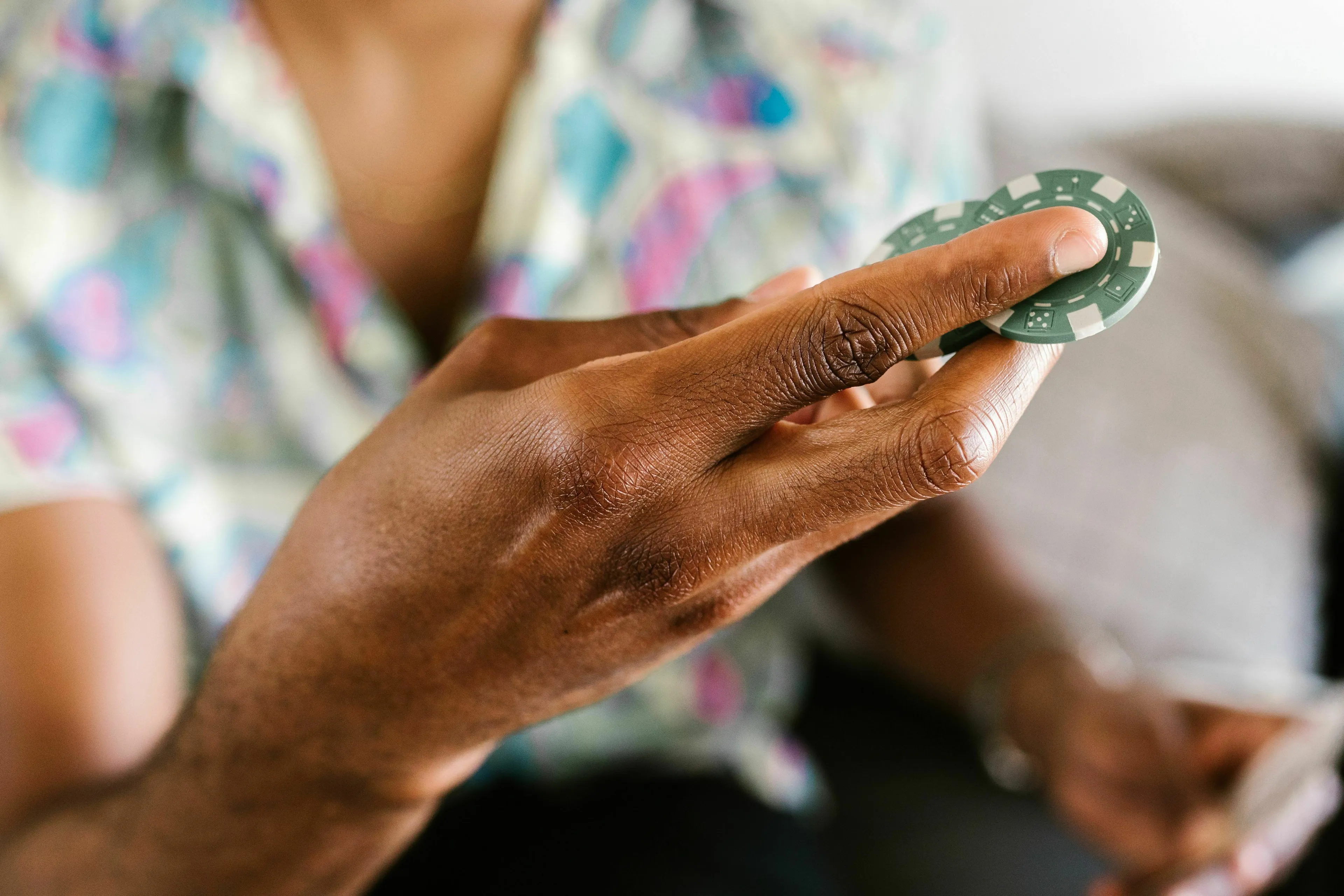A hand holds a green poker chip, considering a mythological trickster's move in a bet.