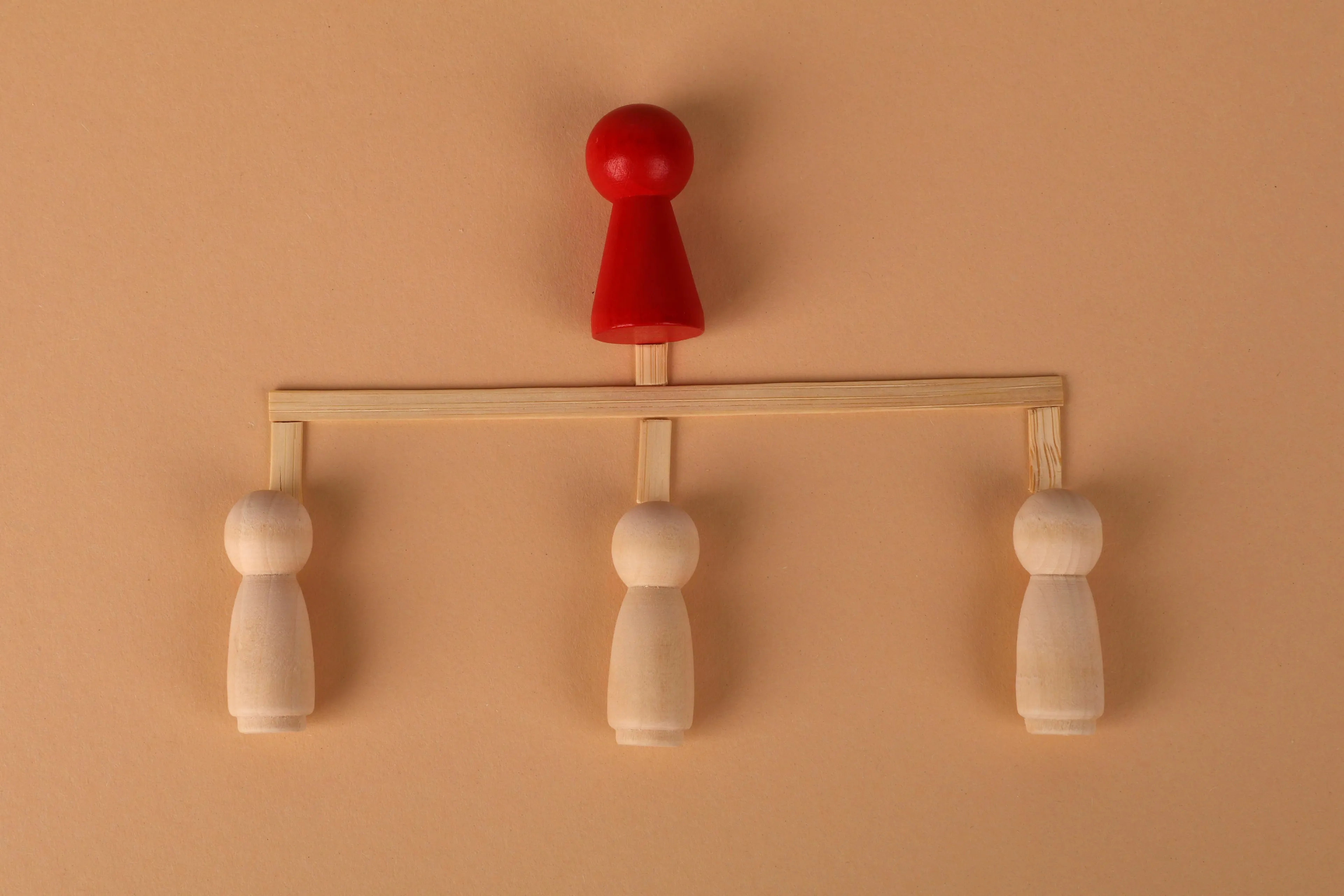 A red wooden pawn figure stands atop a hierarchy of three lighter pawns, representing a mythological trickster's revenge.