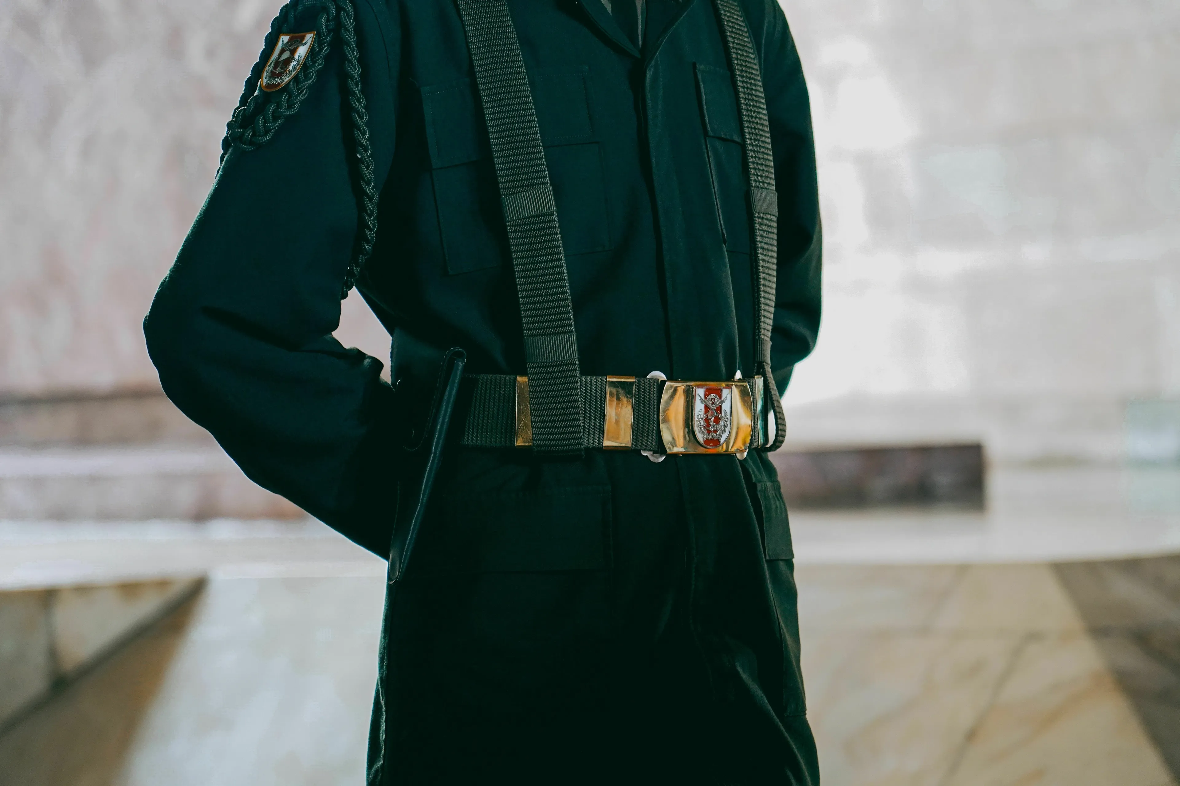 A uniformed guard with a belt and buckle, representing guarding something valuable as a mythological trickster.