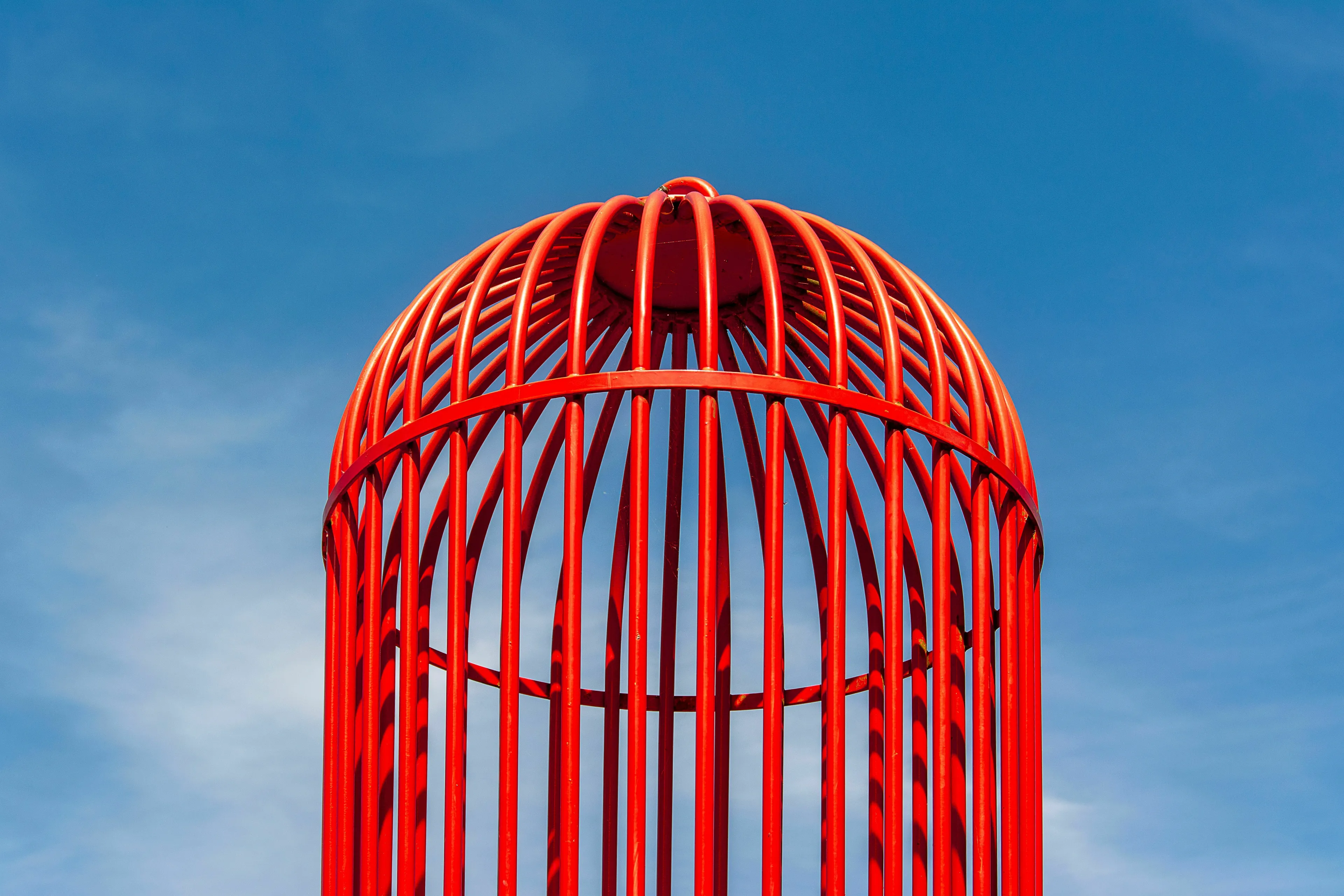 Mythological trickster contemplates escaping a cage against a blue sky.