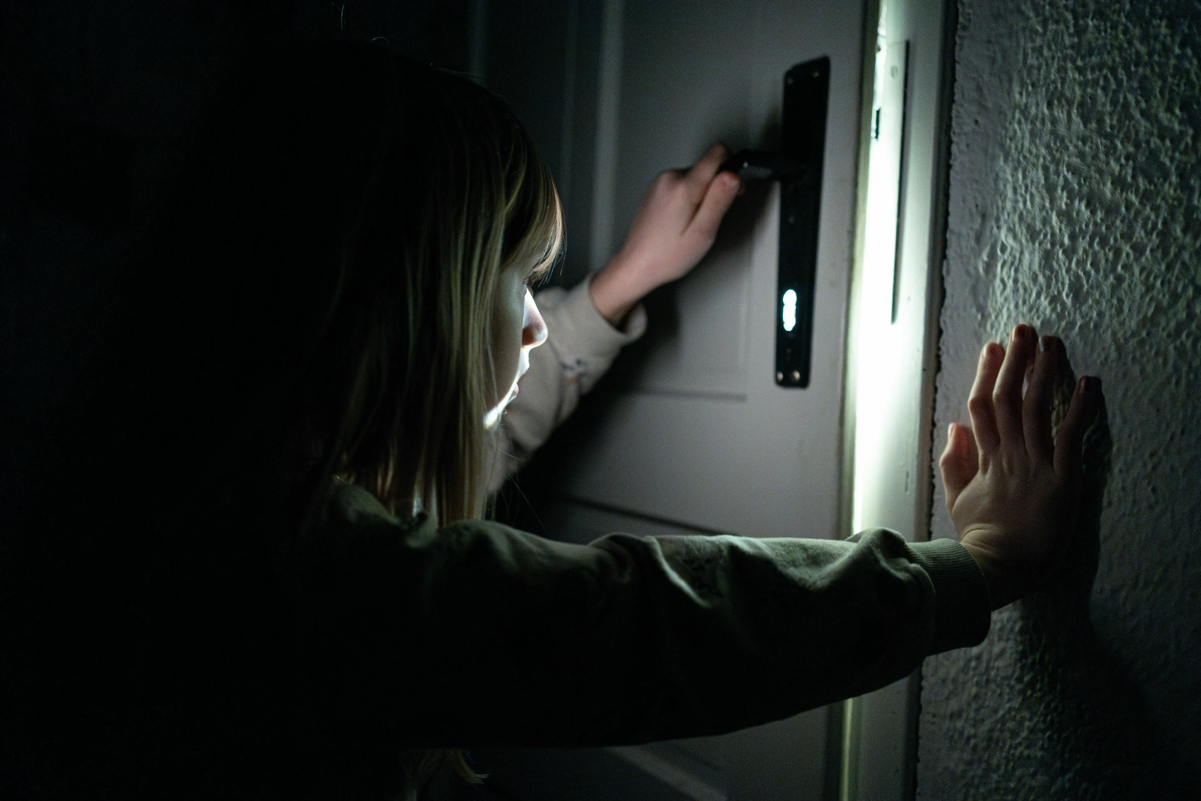 A person shining a light under a door, keeping a powerful secret in a mythological trickster scenario.