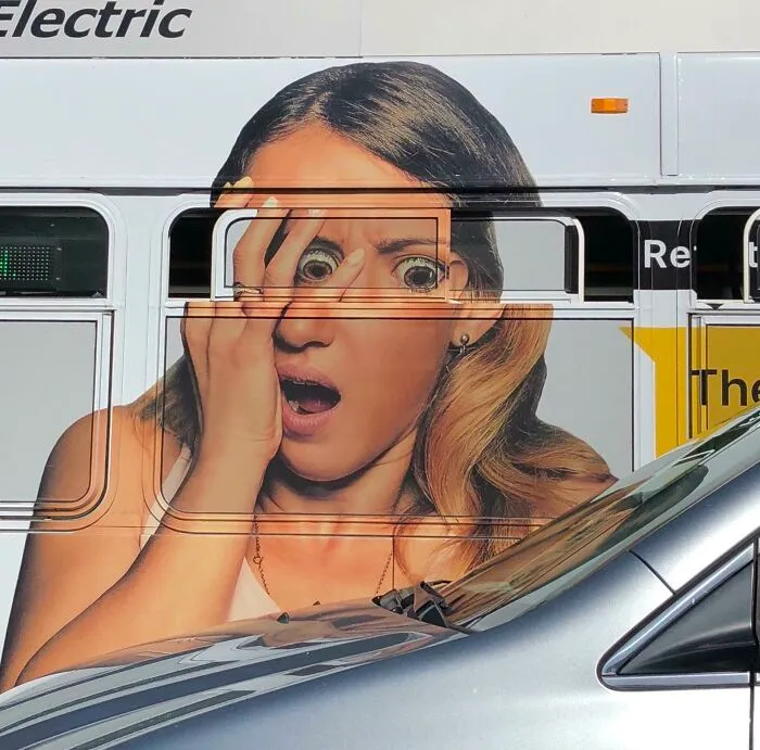 A bus ad showing a woman with her hand covering her face. A window aligns with her eyes, making them look bulging and creating interesting and hilarious ad placement.