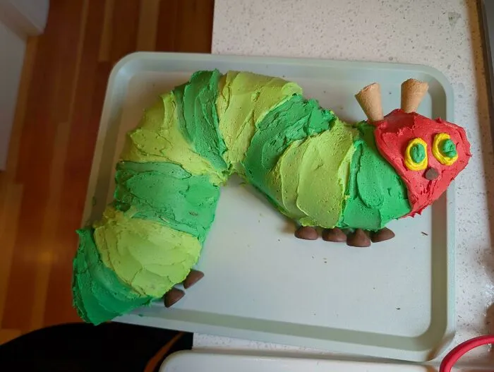 A green and red caterpillar-shaped cake on a white tray. Bakers prove treats look amazing and taste delicious.