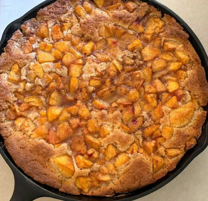A cast iron skillet filled with a baked peach cobbler. Bakers prove treats look amazing and taste delicious.