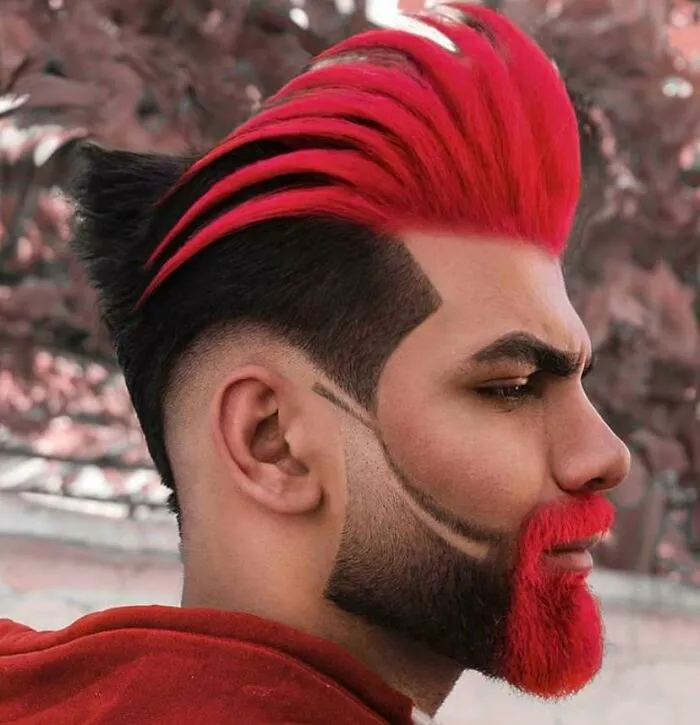 A man with a bold hairstyle, featuring vibrant red spiked hair and a matching red beard.