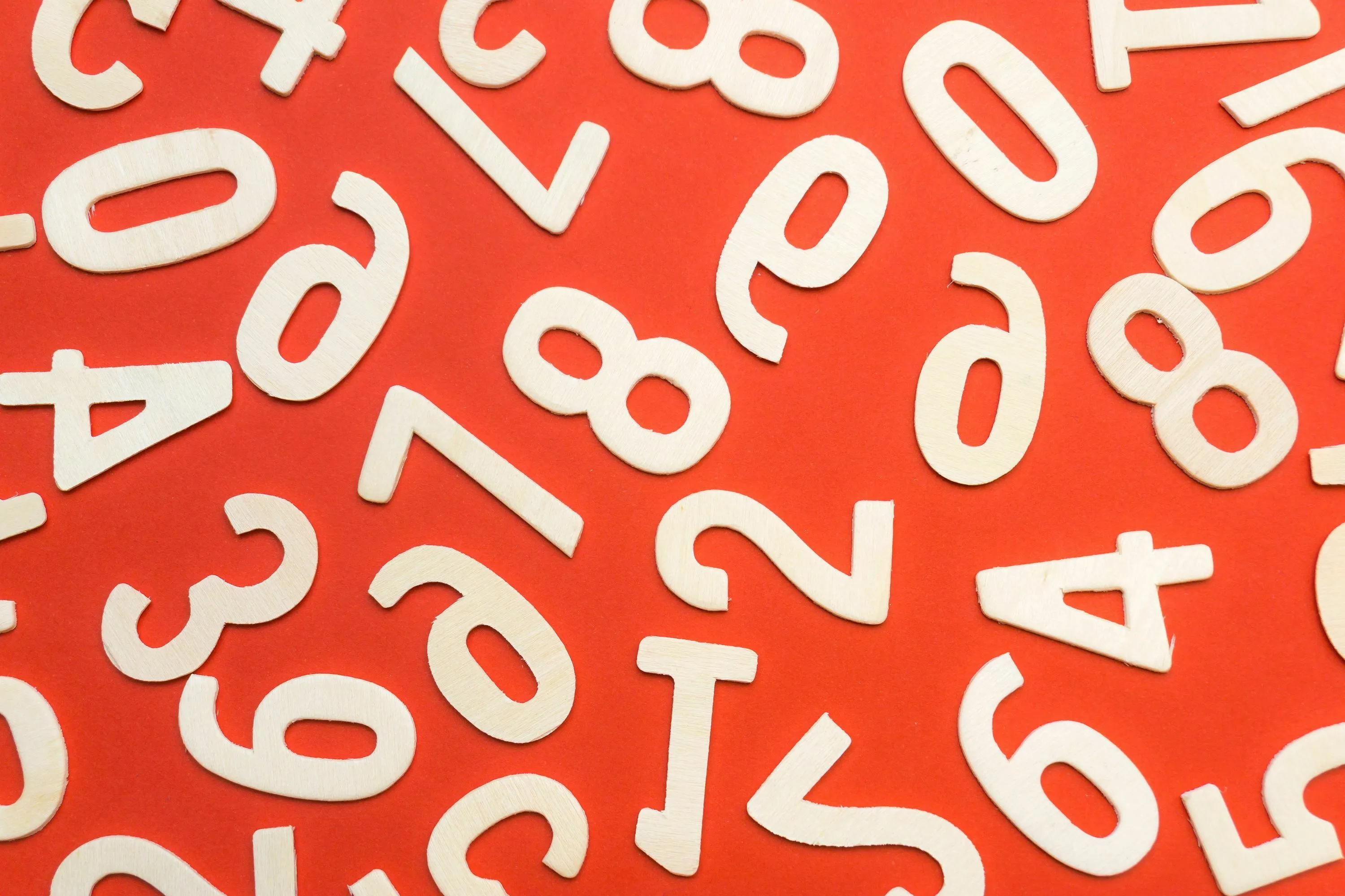 A scattering of wooden numbers on a vibrant red background, representing a pick between 1 and 10 for your Angel Number.