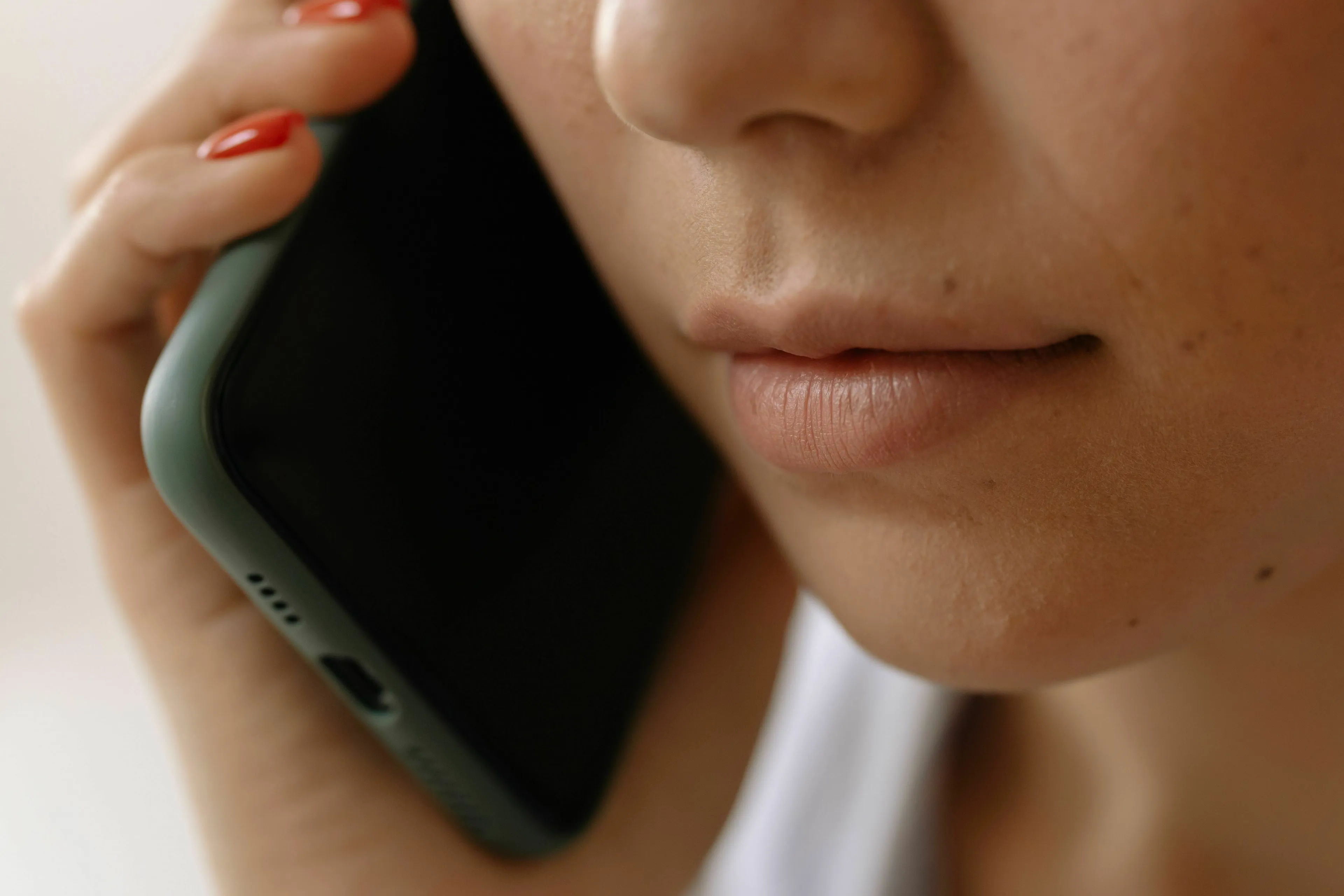 A close-up of a person's mouth and hand holding a phone to their ear, deciding whether to answer an unknown number for their Angel Number.