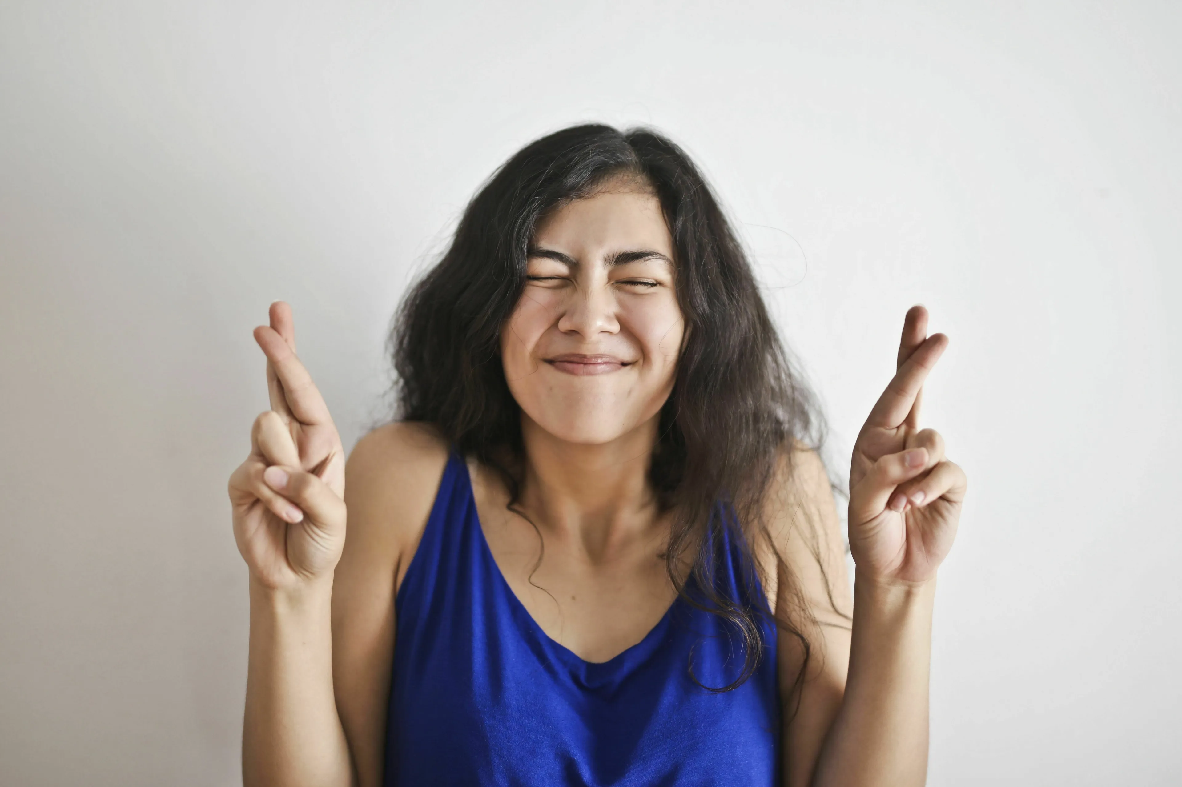 A woman with her eyes closed and fingers crossed, believing in jinxing things. What's Your Angel Number?