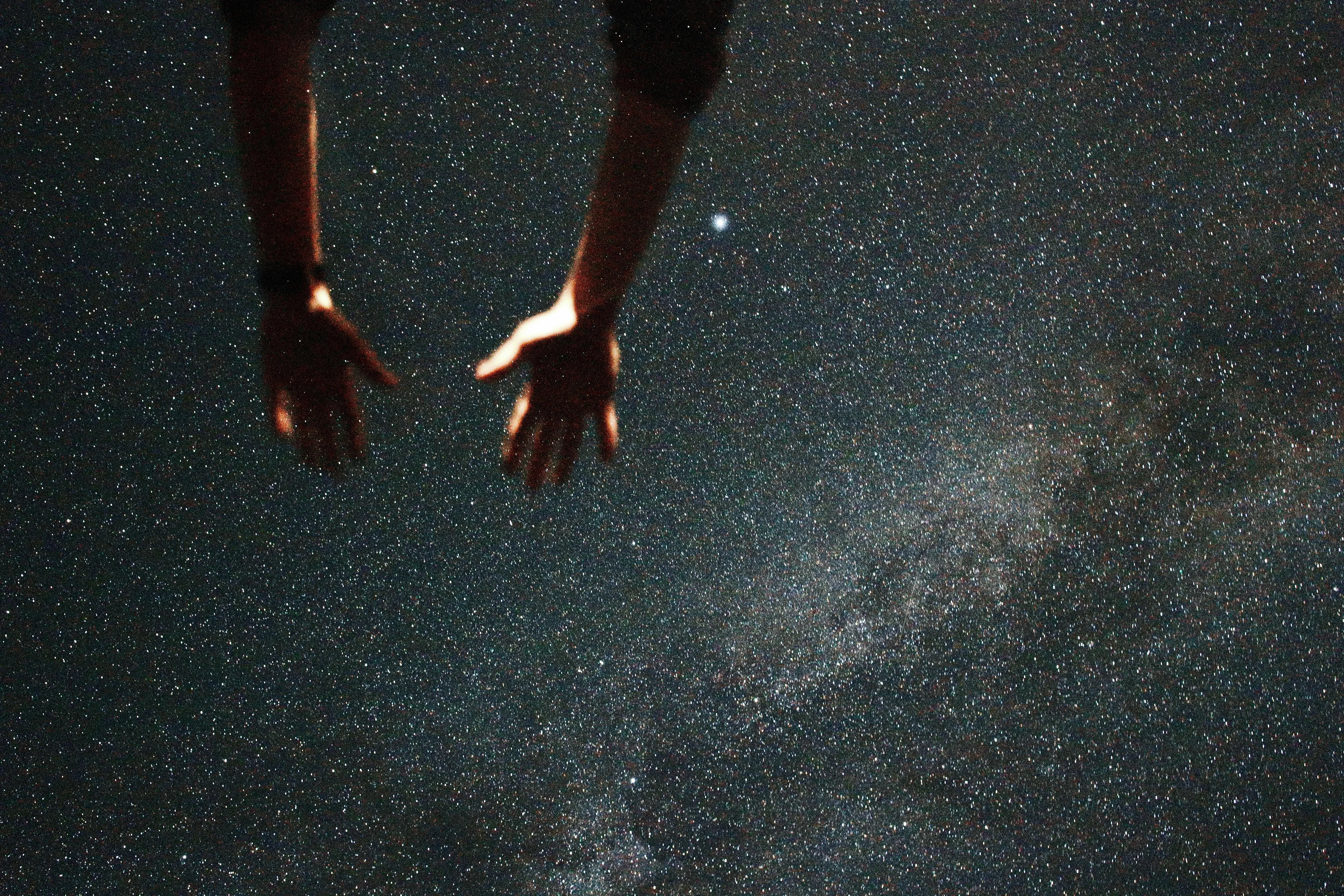 A person reaching towards a starry night sky, contemplating their Angel Number and the universe.