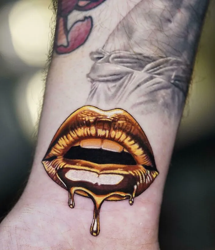 A vibrant tattoo of golden lips with dripping honey on a person's wrist, highlighting stunning tattoos.
