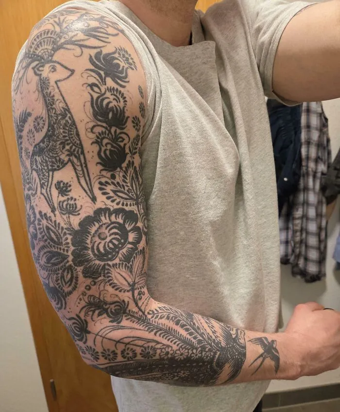 A man's arm with a stunning black and grey floral and animal sleeve tattoo, showing off a happy choice.
