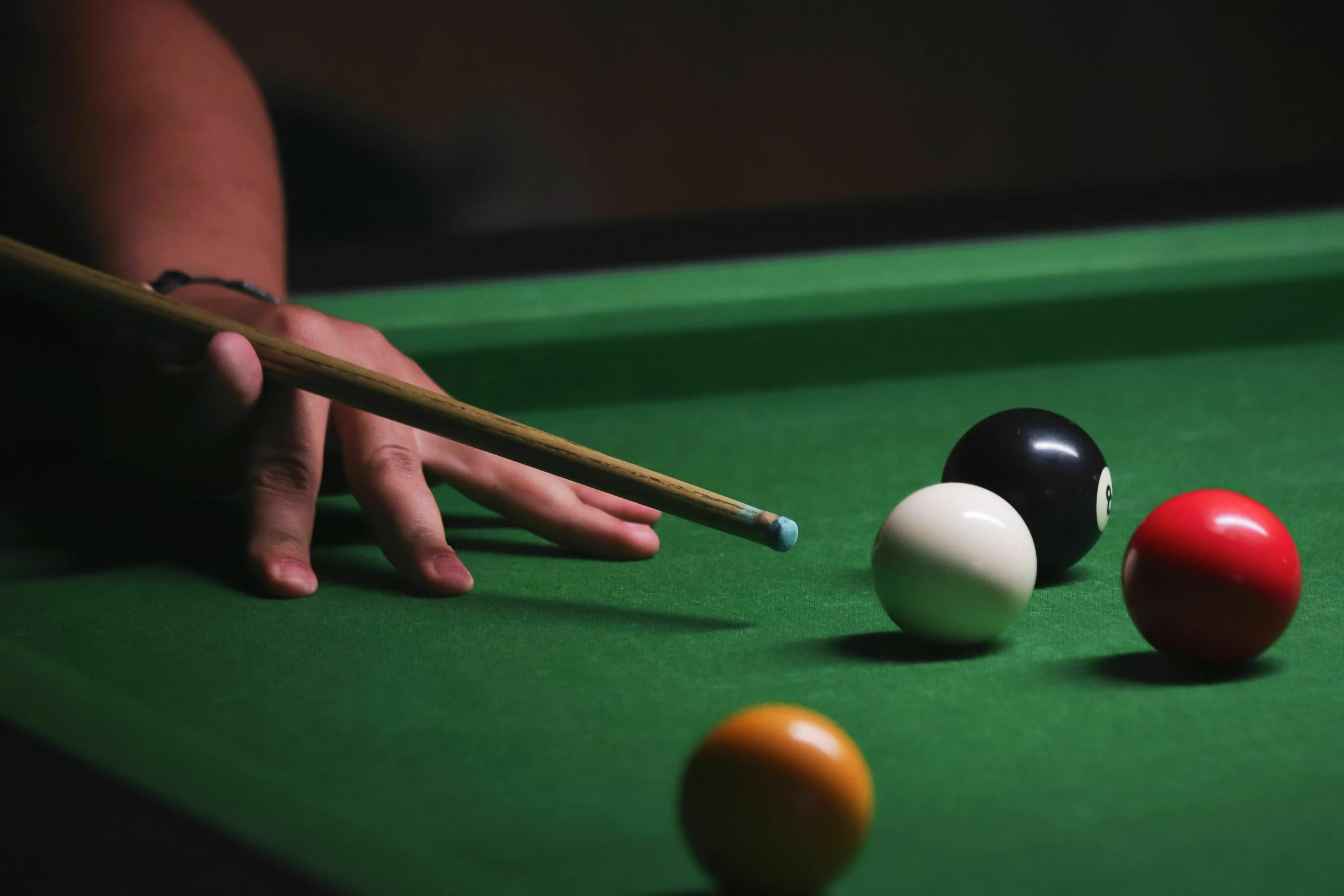 A hand holding a snooker cue, aiming at snooker balls on a green table, for a snooker-related quiz.