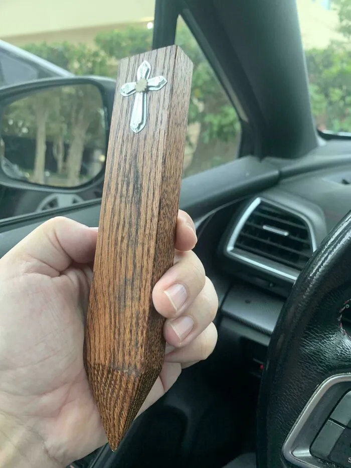 A hand holding a wooden stake with a silver cross, a thrift store jackpot item.