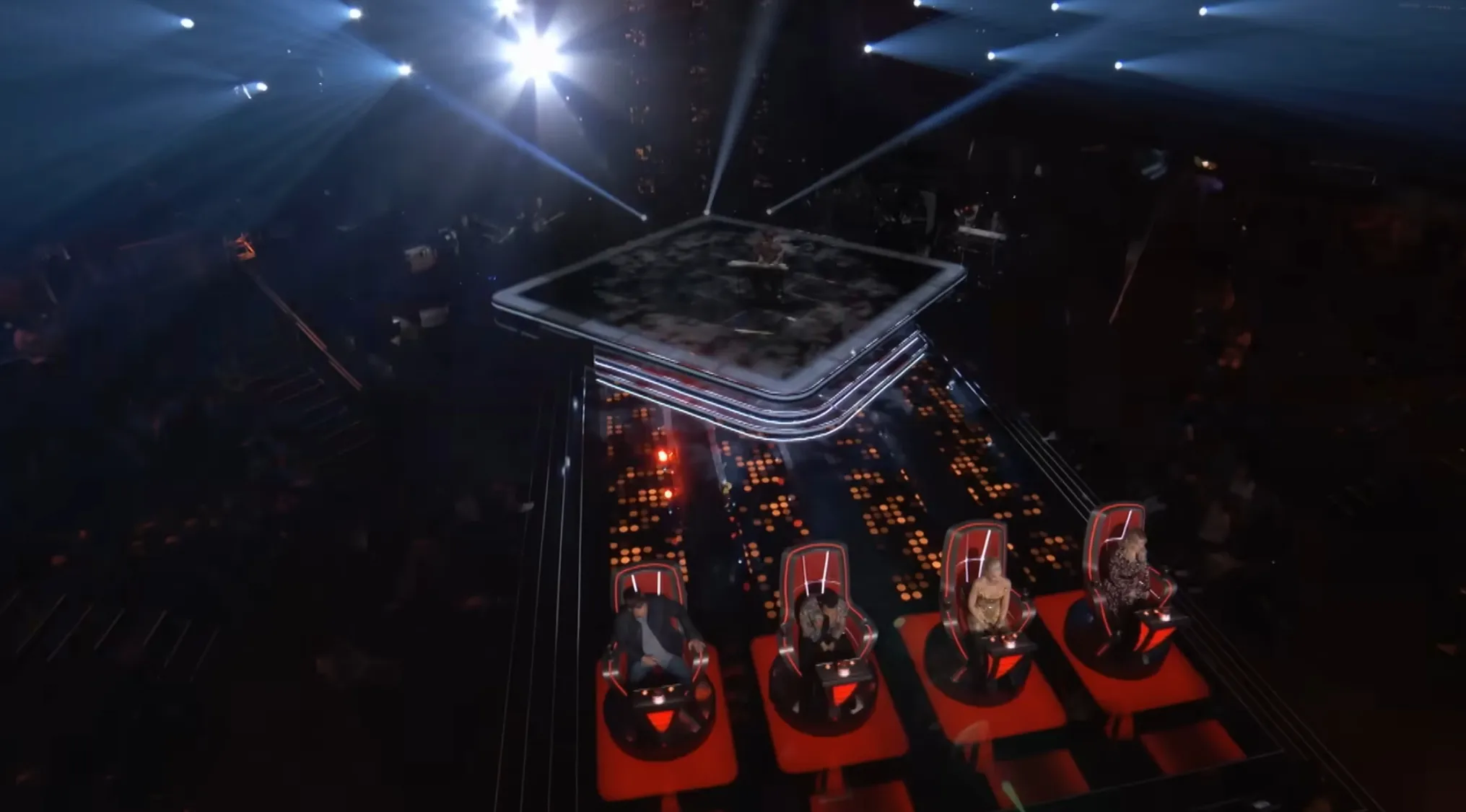 An aerial view of The Voice set with coaches chairs and a brightly lit stage for blind auditions.