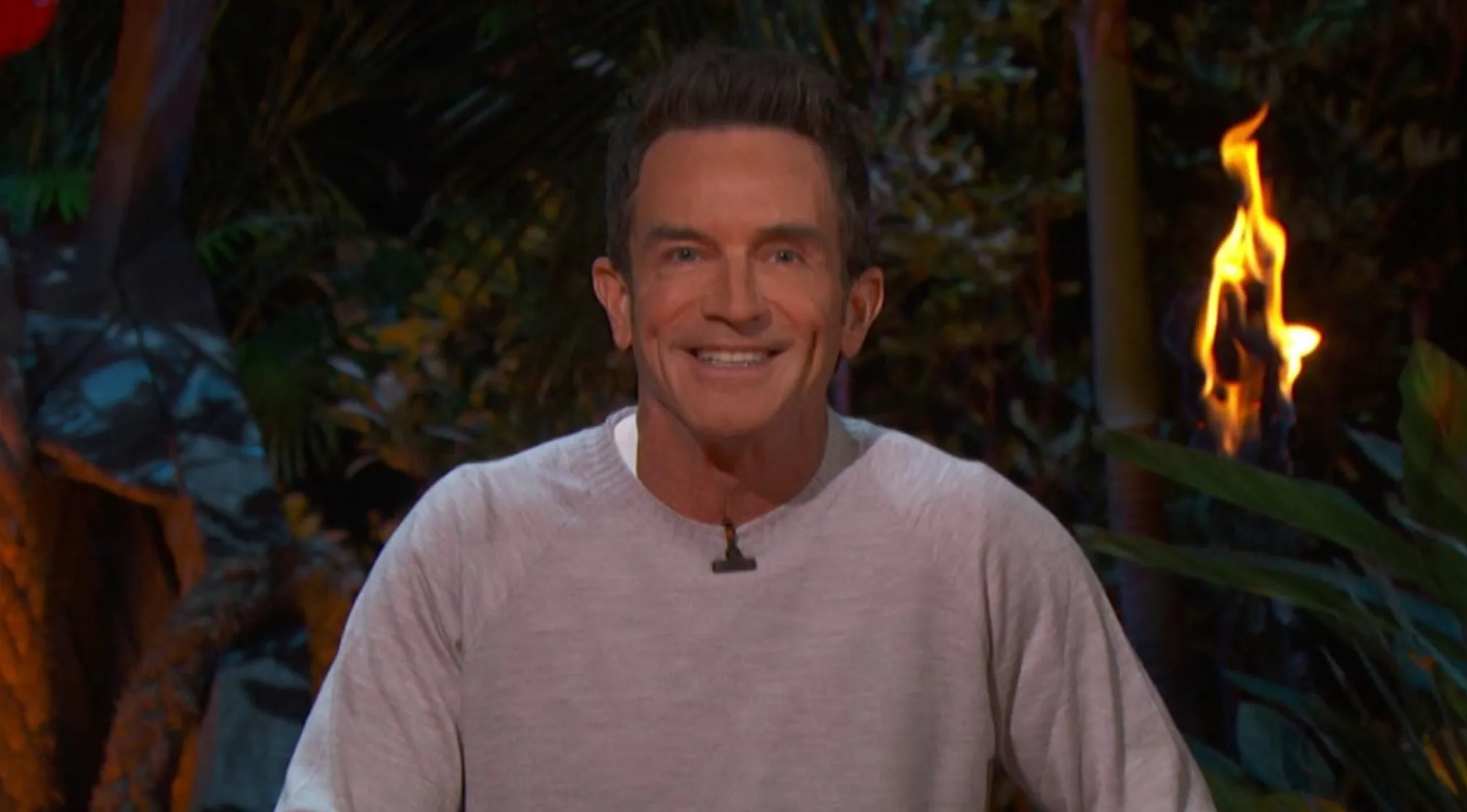 Jeff Probst, the famous host of the reality TV show, smiles with a flaming torch in the background.
