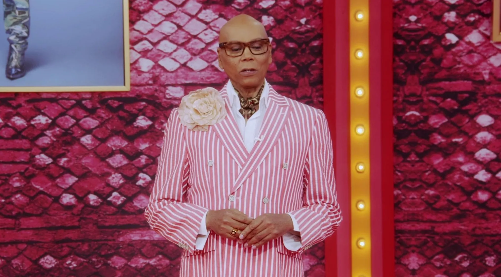 RuPaul, host of the successful Reality TV Show, stands in a pink striped suit.