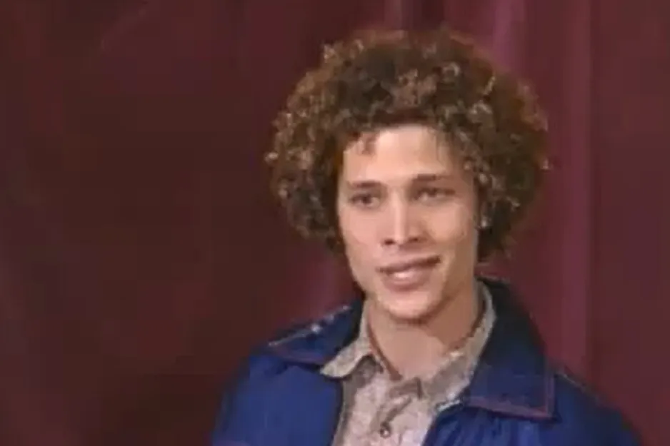 Justin Guarini, with curly hair, smiling as a contestant on American Idol.