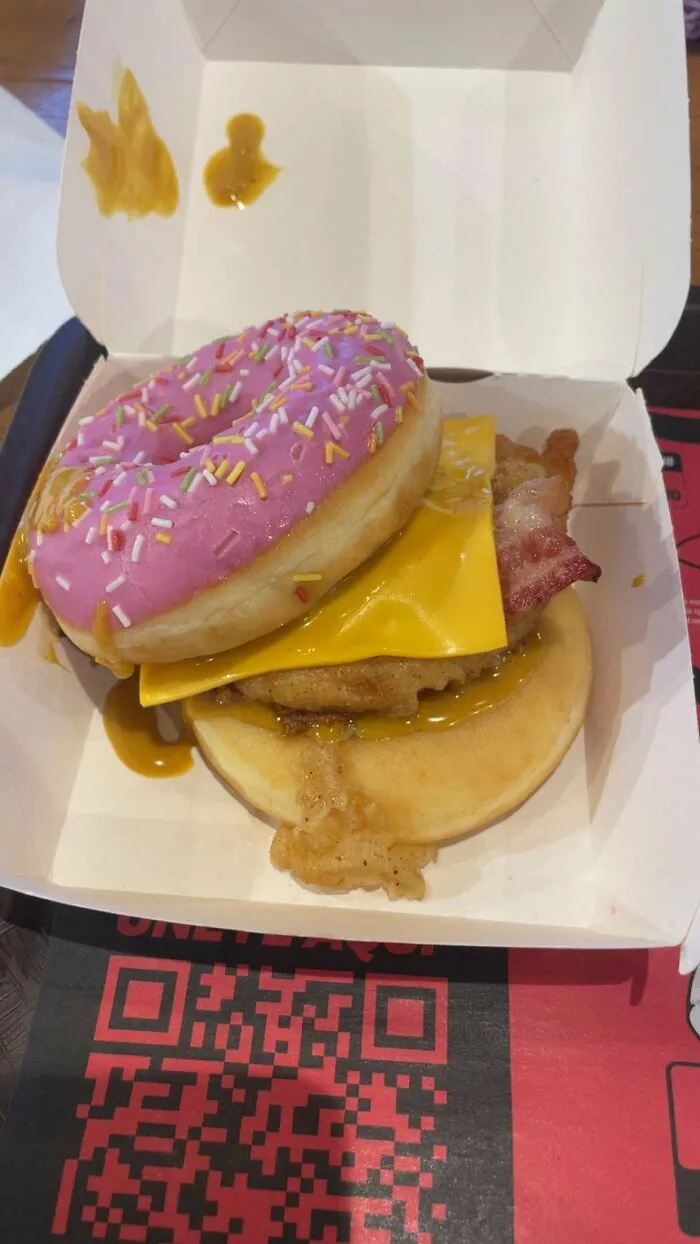 Chicken patty with cheese and bacon inside a frosted sprinkled donut bun, a questionable food combo.