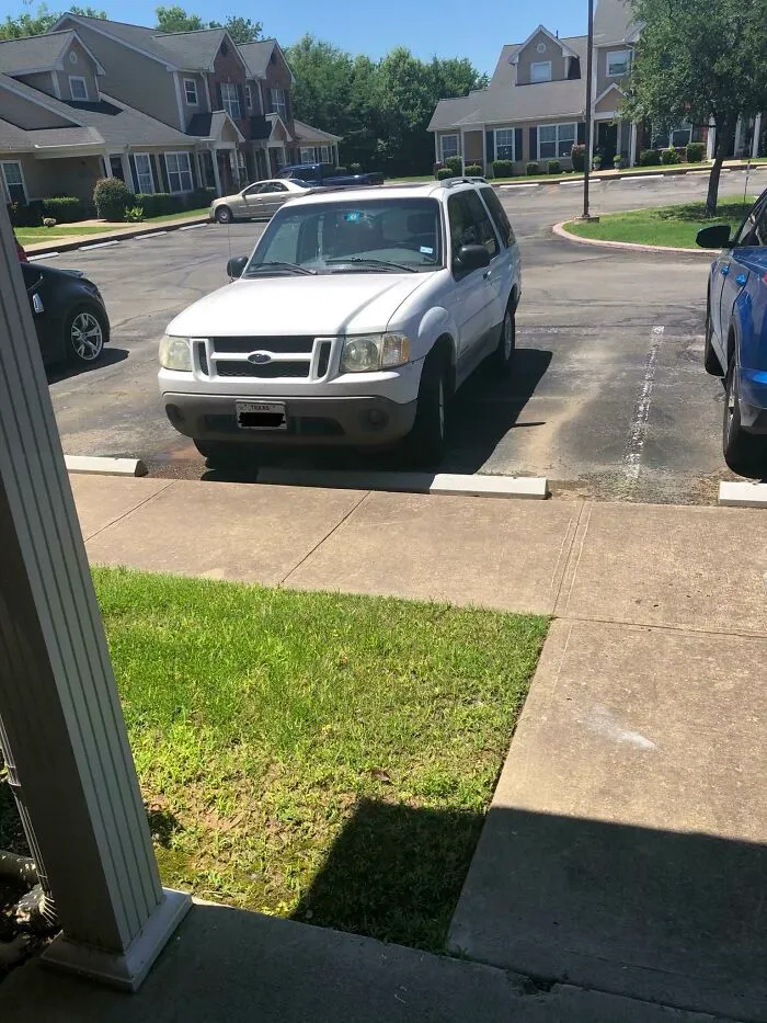 A white SUV, belonging to a jerk neighbor, is parked over the sidewalk and encroaching on the grass.